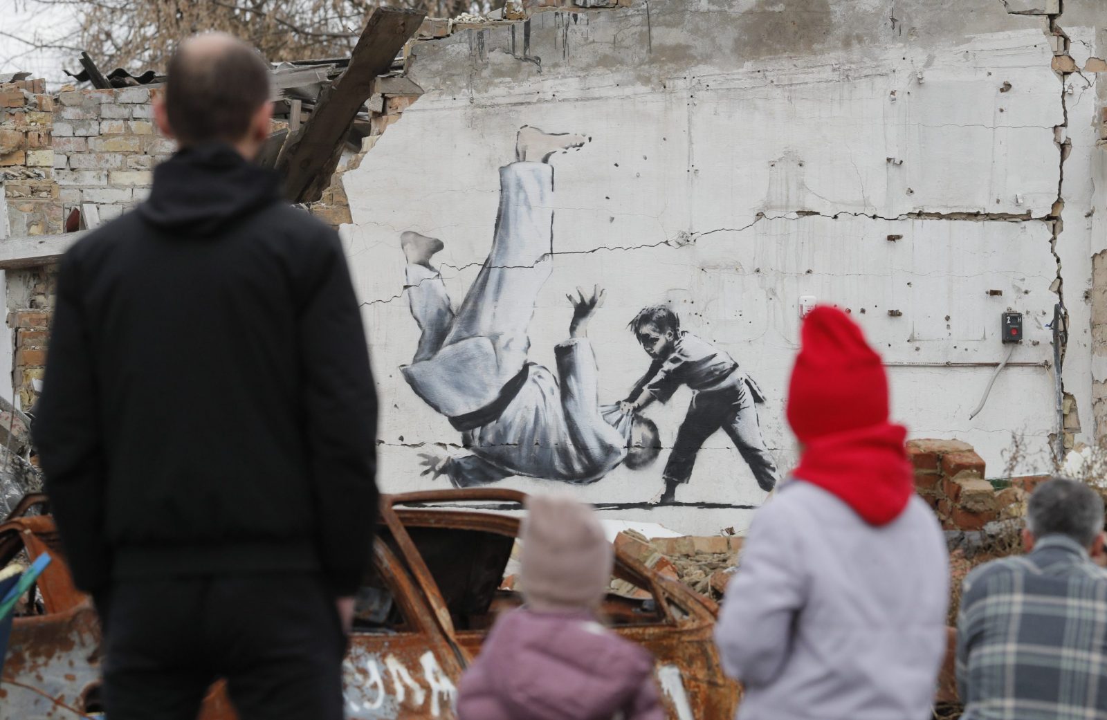 epa10303684 People watch a mural depicting child overthrowing a man in judo clothes, in a style resembling the works of British street artist Banksy, at a wall of a building that was destroyed during shelling in Borodyanka, Ukraine, 13 November 2022. A photo of a mural in Borodyanka depicting a gymnast was shared by Banksy on his social media channel on 11 November, while other works attributed to him in different locations in Ukraine and resembling Banksy's style have not been shared on the artist's channel yet. Russian troops entered Ukraine on 24 February 2022, starting a conflict that has provoked destruction and a humanitarian crisis.  EPA/SERGEY DOLZHENKO