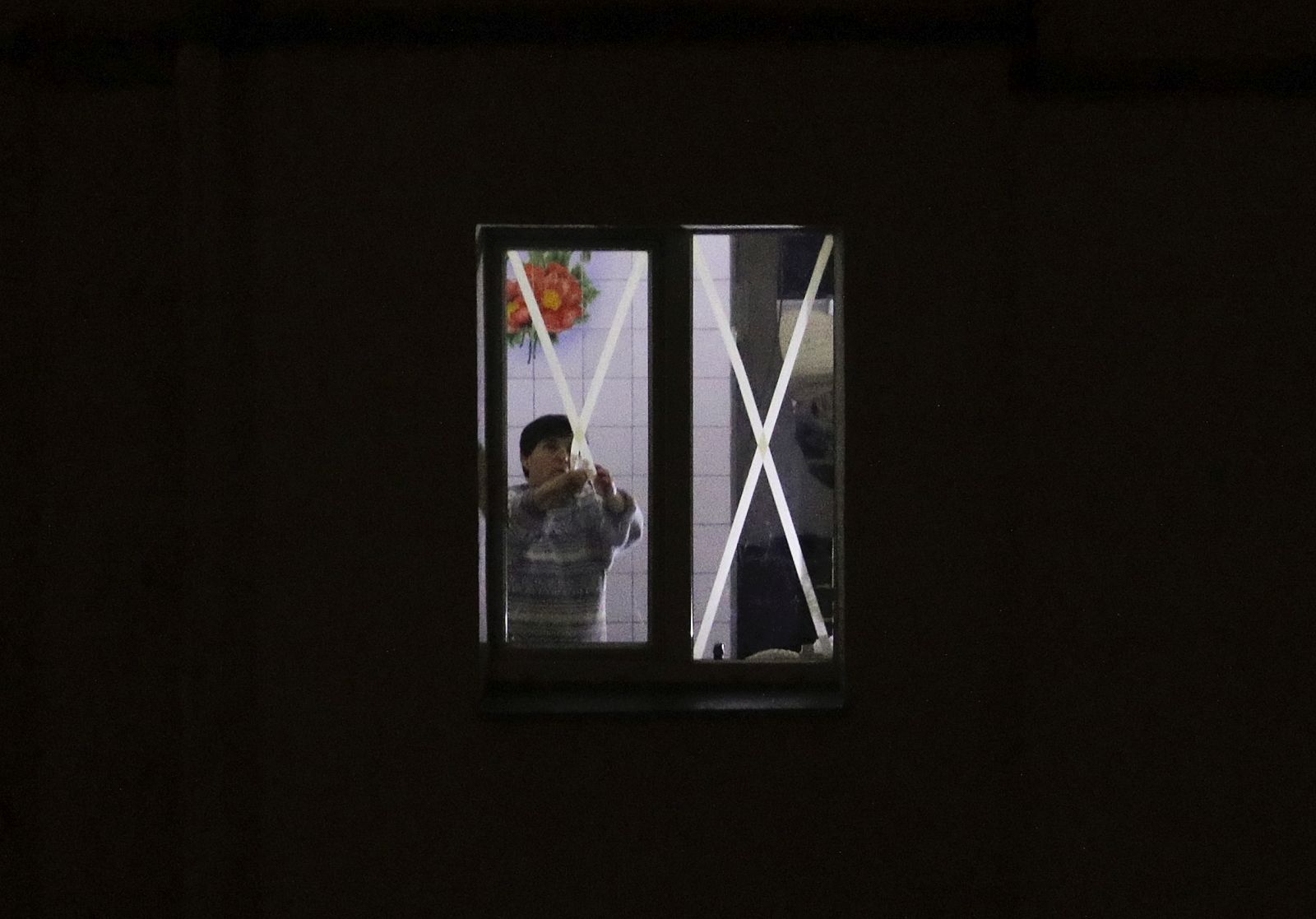 epa10357257 A woman removes tape stripes from a window, used as a protection against glass debris during shelling, in a flat illuminated by offline lighting during the electricity blackout in a residential building in Kyiv, Ukraine, 09 December 2022, amid the Russian invasion. Russia carried out another massive rocket attack against critical infrastructure in several areas of Ukraine on November 23 which provoked the long-term cutting of electricity around all of Ukraine.  EPA/SERGEY DOLZHENKO