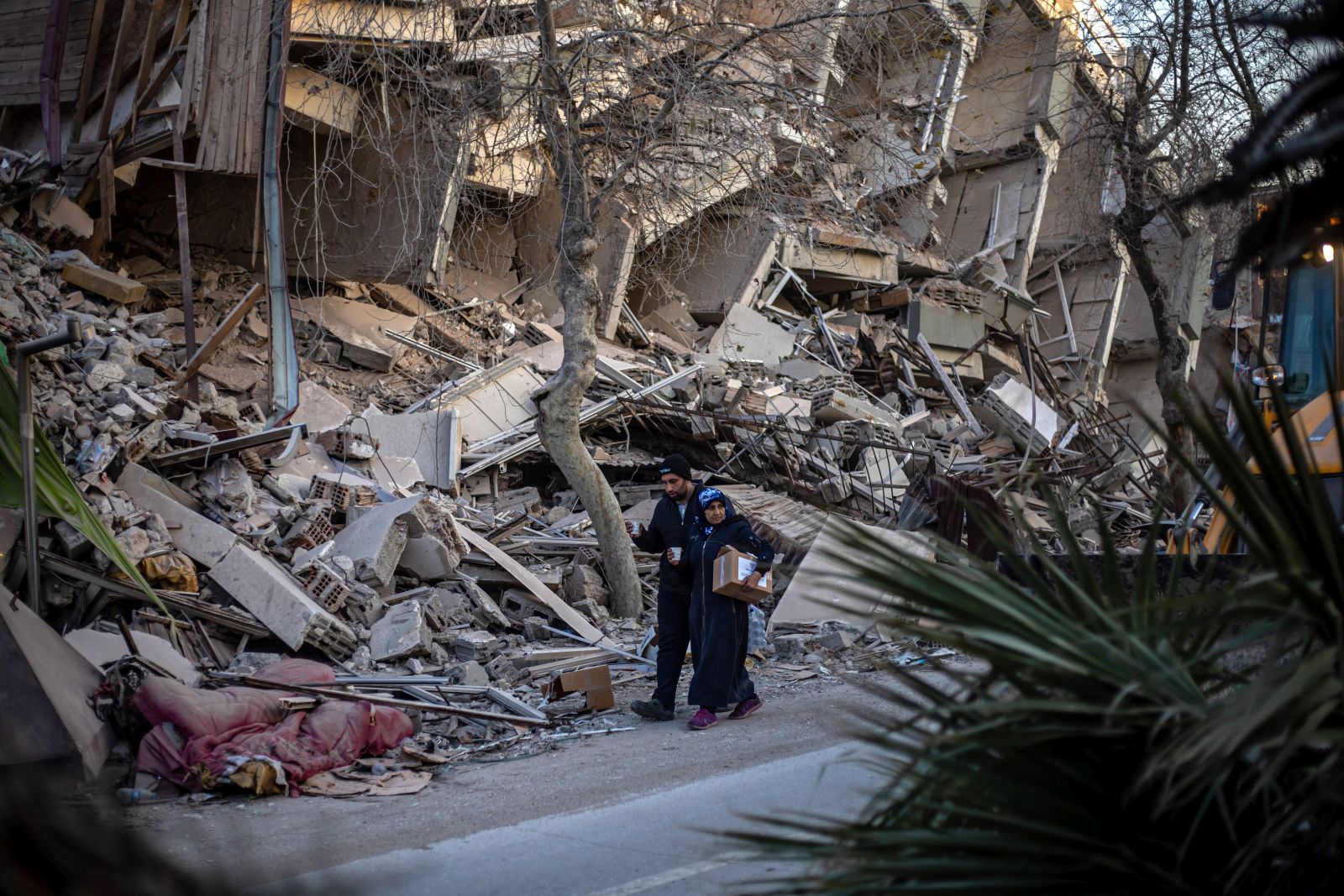 epa10470970 People walk past the site of collapsed buildings after a powerful earthquake, in Hatay, Turkey, 16 February 2023. More than 41,000 people have died and thousands more are injured after two major earthquakes struck southern Turkey and northern Syria on 06 February. Authorities fear the death toll will keep climbing as rescuers look for survivors across the region.  EPA/MARTIN DIVISEK