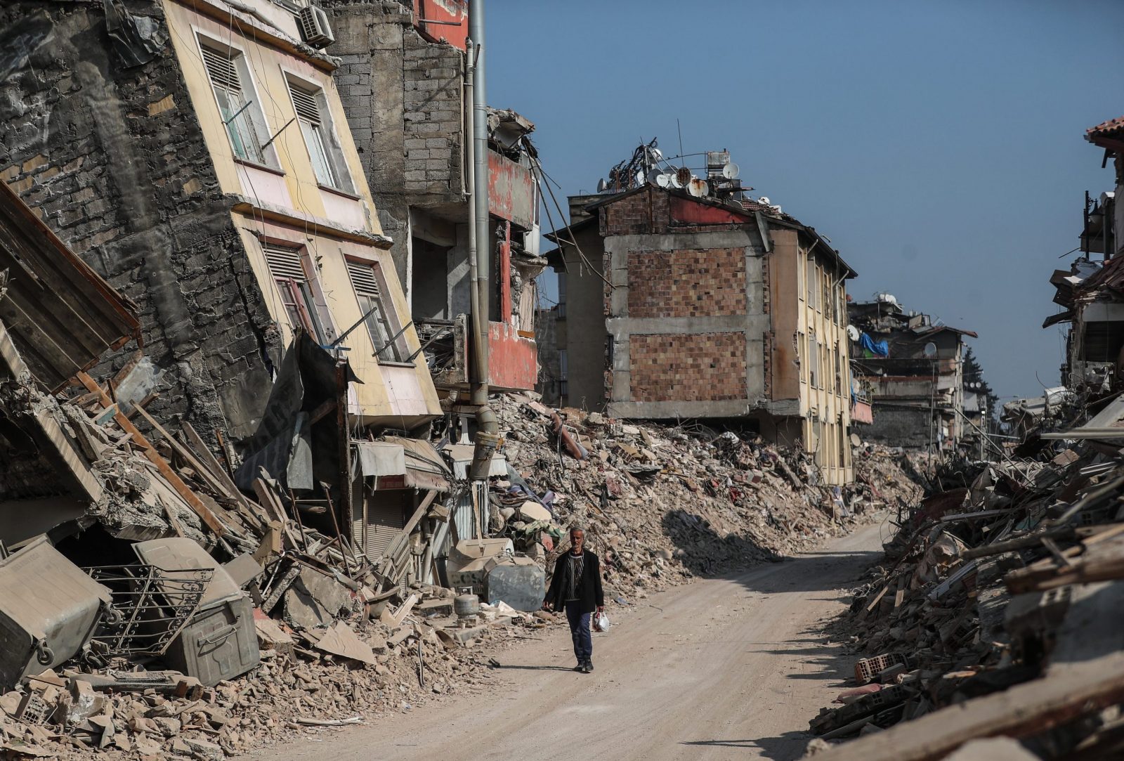 epa10485023 A man walks past collapsed buildings in the aftermath of powerful earthquakes in Hatay, Turkey, 23 February 2023. More than 46,000 people died and thousands more were injured after major earthquakes struck southern Turkey and northern Syria on 06 February and again on 20 February.  EPA/ERDEM SAHIN
