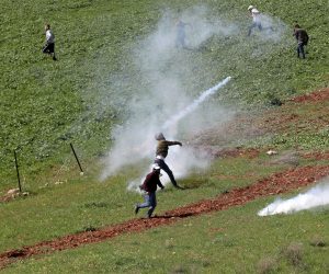 epa10528538 A Palestinian throws back a tear gas grenade as Palestinians seek cover from tear gas during clashes with Israeli soldiers after a protest at Bet Dajan village near the West Bank city of Nablus, 17 March 2023.  EPA/ALAA BADARNEH