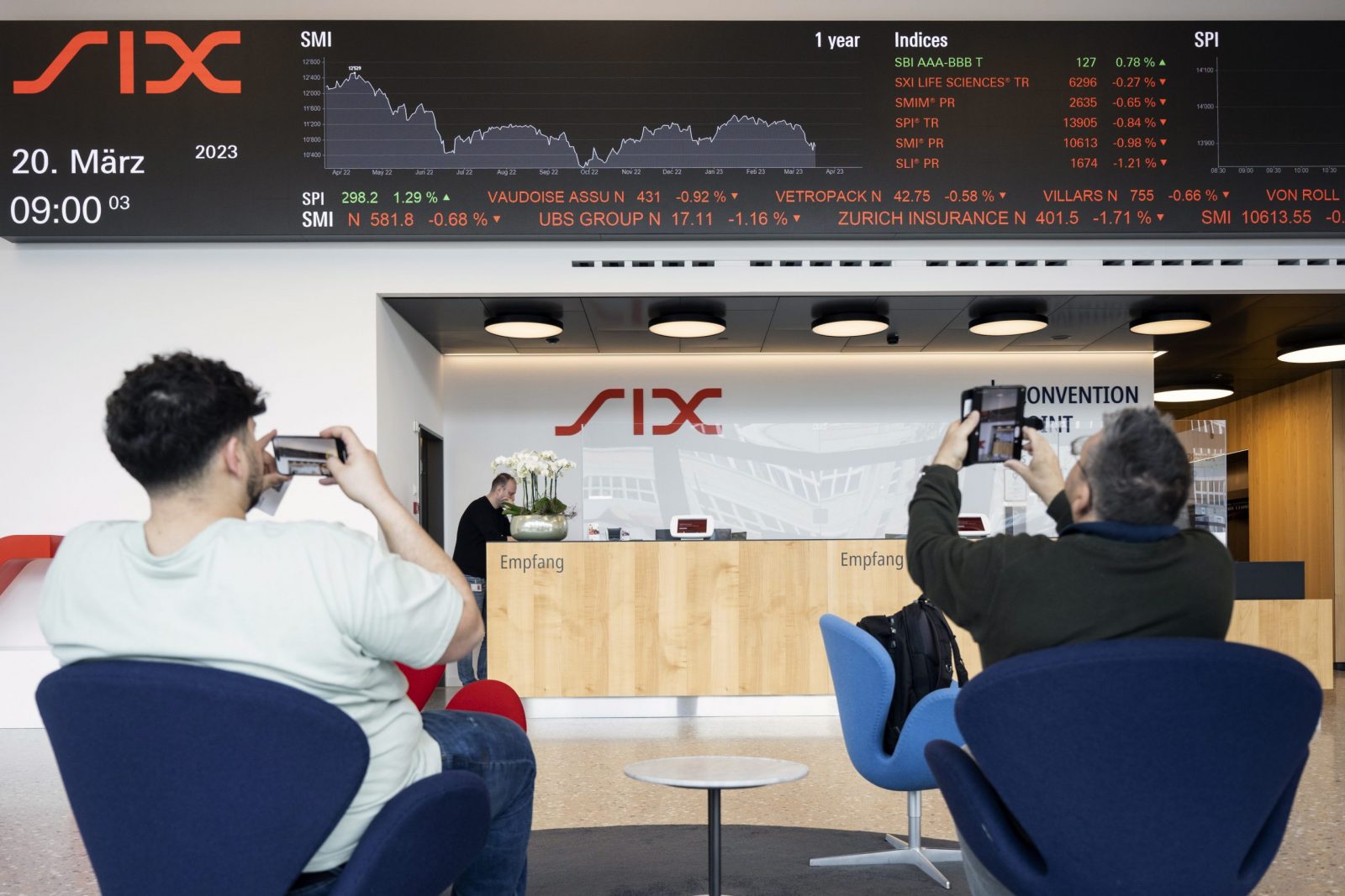 epa10533437 People take photos of a ticker showing the developments on UBS Group stock, among others, at SIX Swiss Exchange in Zurich, Switzerland, 20 March 2023. Financial markets are reacting after troubled bank Credit Suisse was rescued in a three billion dollars purchase by its Swiss rival UBS in a government-backed deal. UBS is down 13 percent and other European bank shares have also dropped significantly.  EPA/ENNIO LEANZA