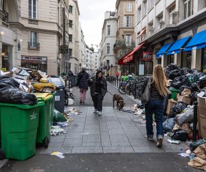 epa10535245 People pass next to garbage cans overflowing with trash in Paris, France, 21 March 2023. Parisian streets are full of more than 9,000 tons of waste yet to be collected after two weeks of garbage collectors' strike, who have joined the massive strikes in France against the government's pension reform plans after French prime minister on 16 March had announced the use of article 49 paragraph 3 (49.3) of the Constitution of France to have the text on the controversial law to be definitively adopted without a vote.  EPA/CHRISTOPHE PETIT TESSON