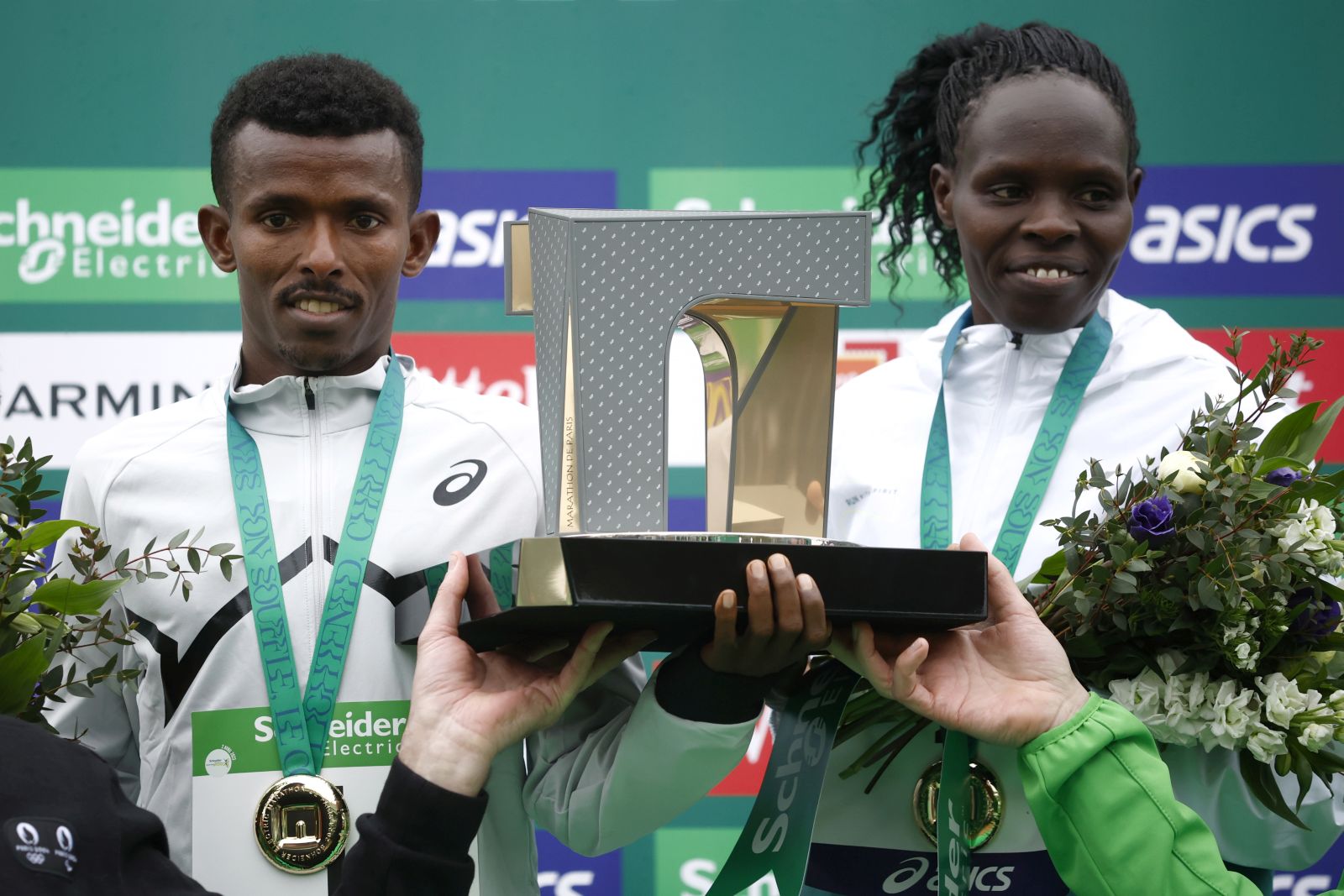 epa10555078 Ethiopian runner Abeje Ayana (L) and Kenyan runner Helah Kiprop (R) celebrate their win on the podium following the 46th edition of the 'Schneider Electric Marathon de Paris 2023’ in Paris, France, 02 April 2023.  EPA/YOAN VALAT