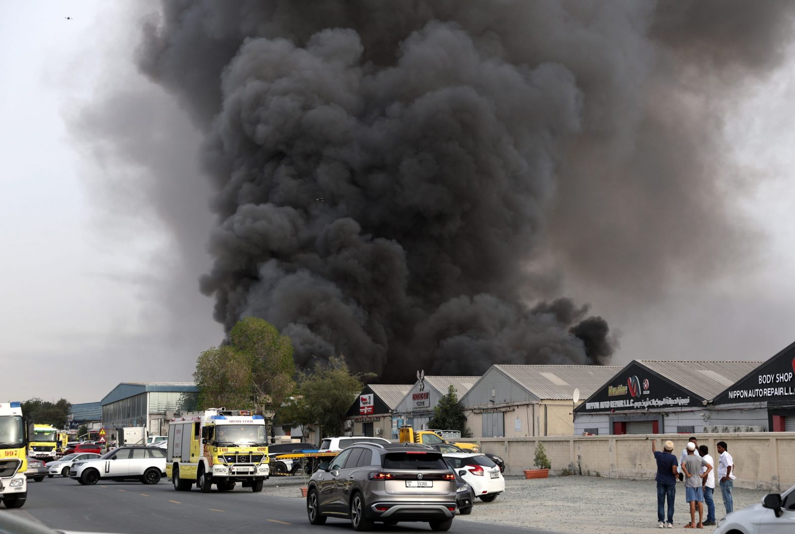 epa10572709 People look at smoke rising from a fire in a warehouse at Umm Ramool, a residential and commercial community in the Gulf emirate of Dubai, United Arab Emirates, 14 April 2023. The fire broke off at a warehouse that contained cleaning material, according to an announcement by the Dubai Civil Defense.  EPA/ALI HAIDER