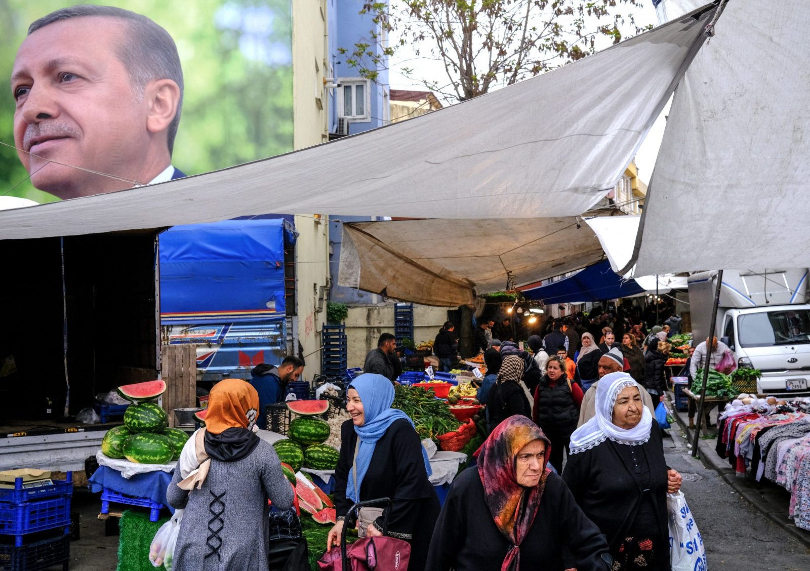 epa10610611 People shop at Kasimpasa neighborhood's local market with a picture of Turkish President Recep Tayyip Erdogan in the background, in Istanbul, Turkey, 05 May 2023. General elections will be held in Turkey on 14 May 2023 with a two-round voting to elect the President of Turkey and parliamentary elections held simultaneously to elect the members of the Grand National Assembly of Turkey.  EPA/SEDAT SUNA