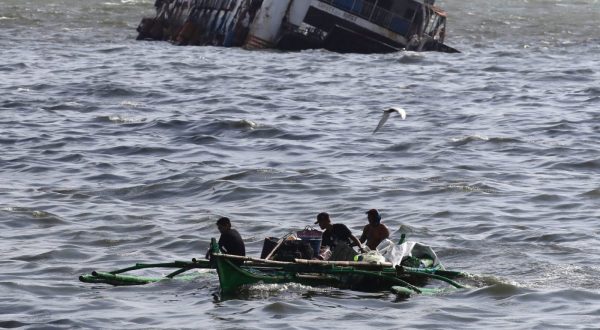 epa10663097 Filipino fishermen on a boat maneuver on rough seas next to a half submerged ship in the waters of Manila Bay, Philippines, 30 May 2023. As a precaution of approaching Typhoon Mawar, Philippine government authorities have evacuated thousands of residents, imposed a no-sail ban, suspended school classes, and shutdown offices in the northern part of Luzon island, the country’s largest and most populous island.  EPA/FRANCIS R. MALASIG