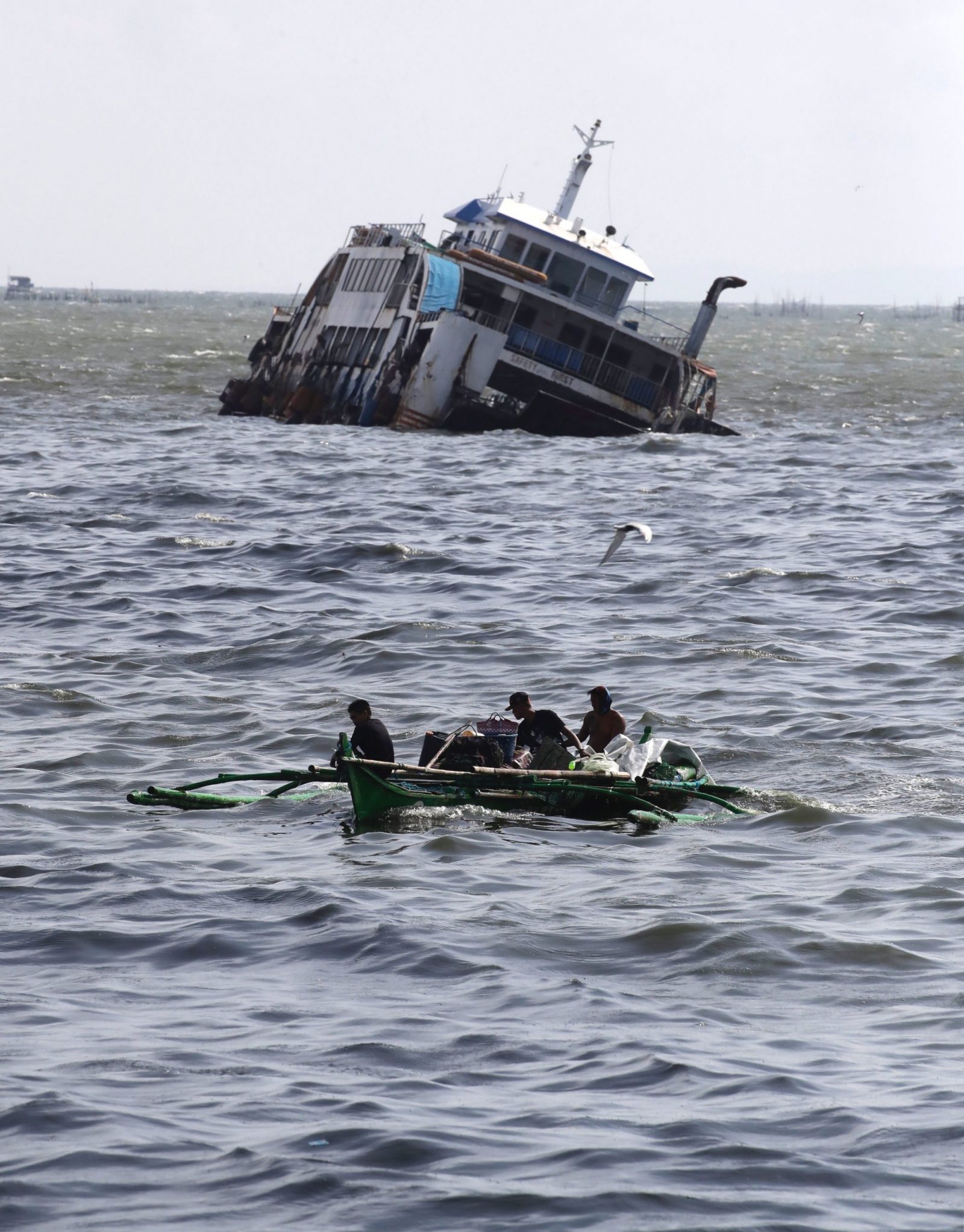 epa10663097 Filipino fishermen on a boat maneuver on rough seas next to a half submerged ship in the waters of Manila Bay, Philippines, 30 May 2023. As a precaution of approaching Typhoon Mawar, Philippine government authorities have evacuated thousands of residents, imposed a no-sail ban, suspended school classes, and shutdown offices in the northern part of Luzon island, the country’s largest and most populous island.  EPA/FRANCIS R. MALASIG