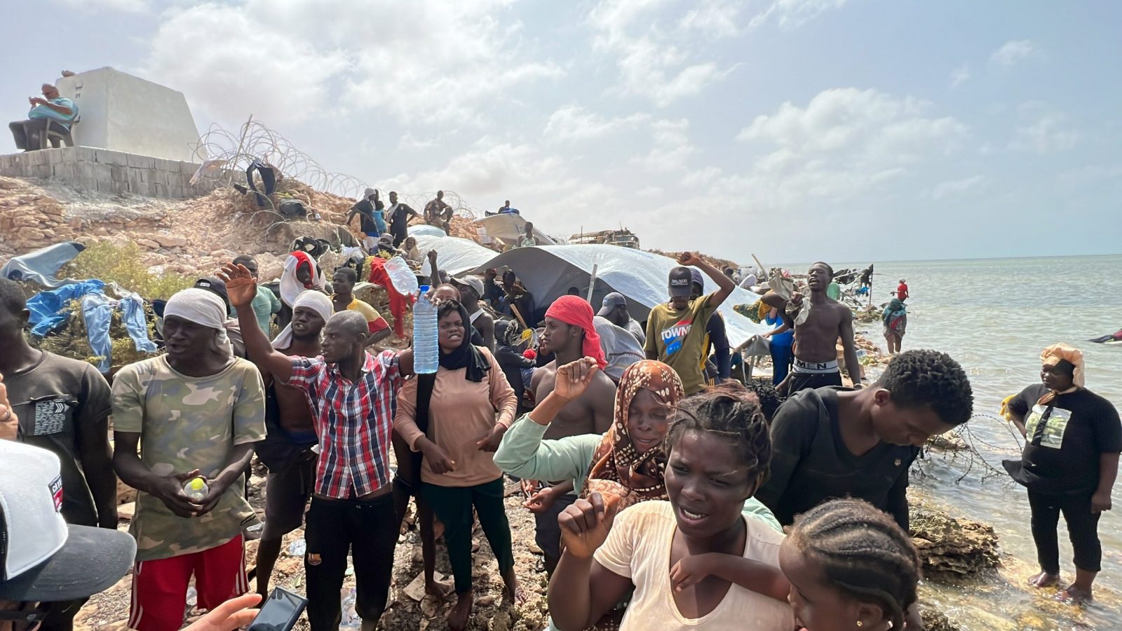 epa10770032 Sub-Saharan African migrants who were expelled from the city of Sfax in Tunisia gather in an area near the Libyan-Tunisia border, in Ras Jedir, 173 km west of Tripoli, Libya, 26 July 2023. Libyan border guards found some 150 people, women, children and families stranded in scorching summer temperatures and without water. According to the Red Crescent, Tunisian security forces have moved hundreds of migrants into the arid zone since June 2023.  EPA/STR