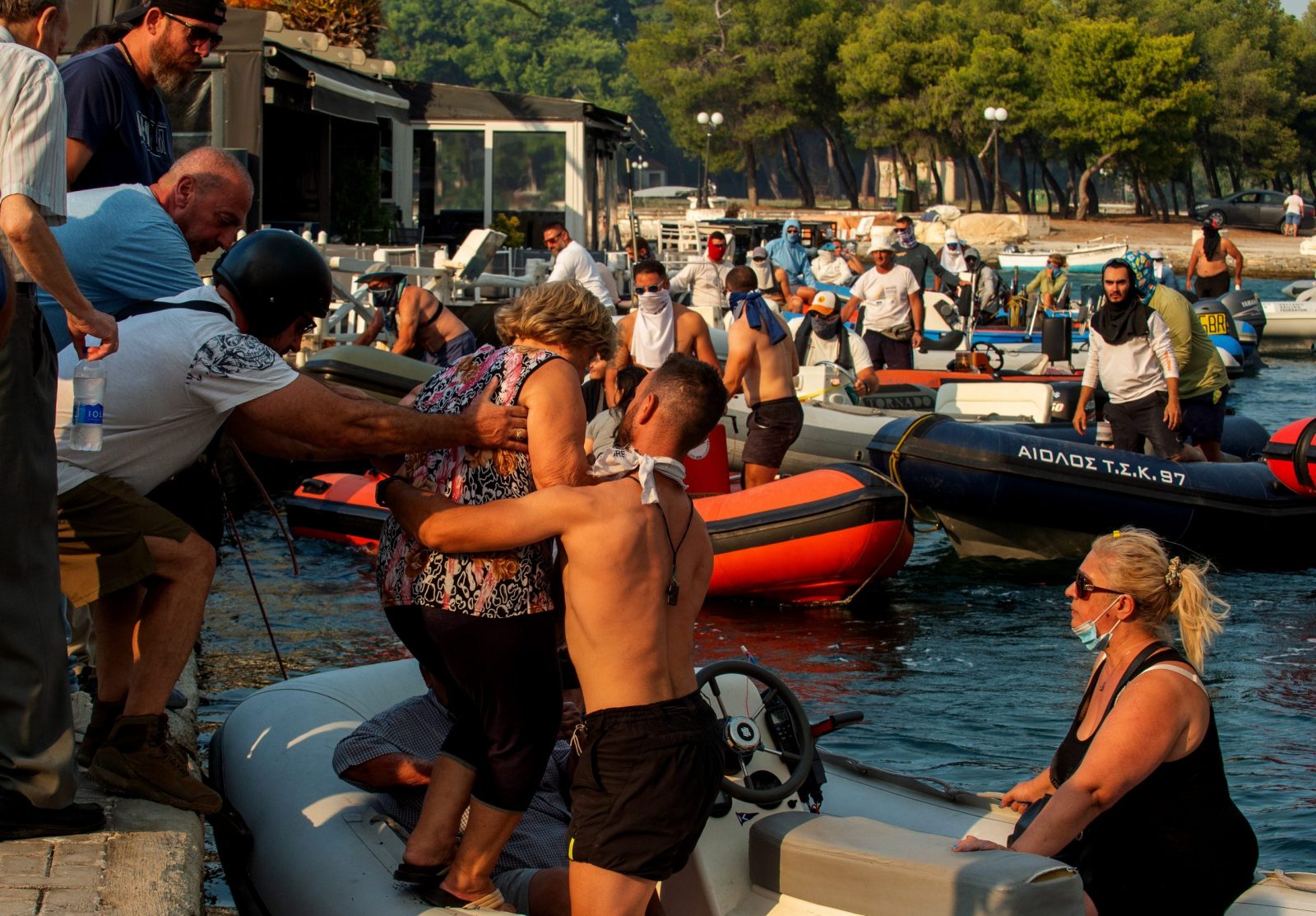 epa10772158 People evacuate by boats during a wildfire at Nea Anchialos, near Volos, Greece 27 July 2023. Explosions occurred at a munitions depot at Nea Anchialos base of the Hellenic Airforce near Volos in the afternoon of 27 July. According to authorities, the blast happened following a fire that had started in the Volos area and spread to the military airport, which functions as the base for the Tactical Air Force's 111 Combat Wing.  EPA/IKONOMOU VASSILIS