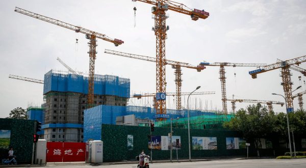 epa10820811 A woman rides an electric scooter next to a construction site of a housing and commercial establishment in Beijing, China, 26 August 2023. China has approved guidelines for the planning and construction of affordable housing during a meeting chaired by China's Premier Li Qiang. The guidlines were developed in order to promote the development of the property market, as the country continues to revive the economy following the Covid pandemic.  EPA/MARK R. CRISTINO