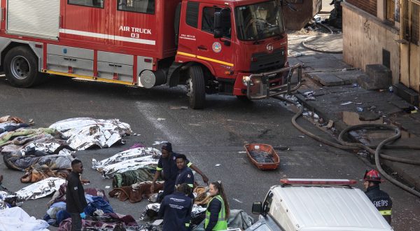 epa10830422 Fire crews and emergency staff stand next to the covered bodies of the victims as they gather at the site of a fire that broke out at the five-storey building in the city centre, in Johannesburg, South Africa, 31 August 2023. More than 60 people have died following a fire that ravaged a building in central Johannesburg according to officials.  EPA/KIM LUDBROOK