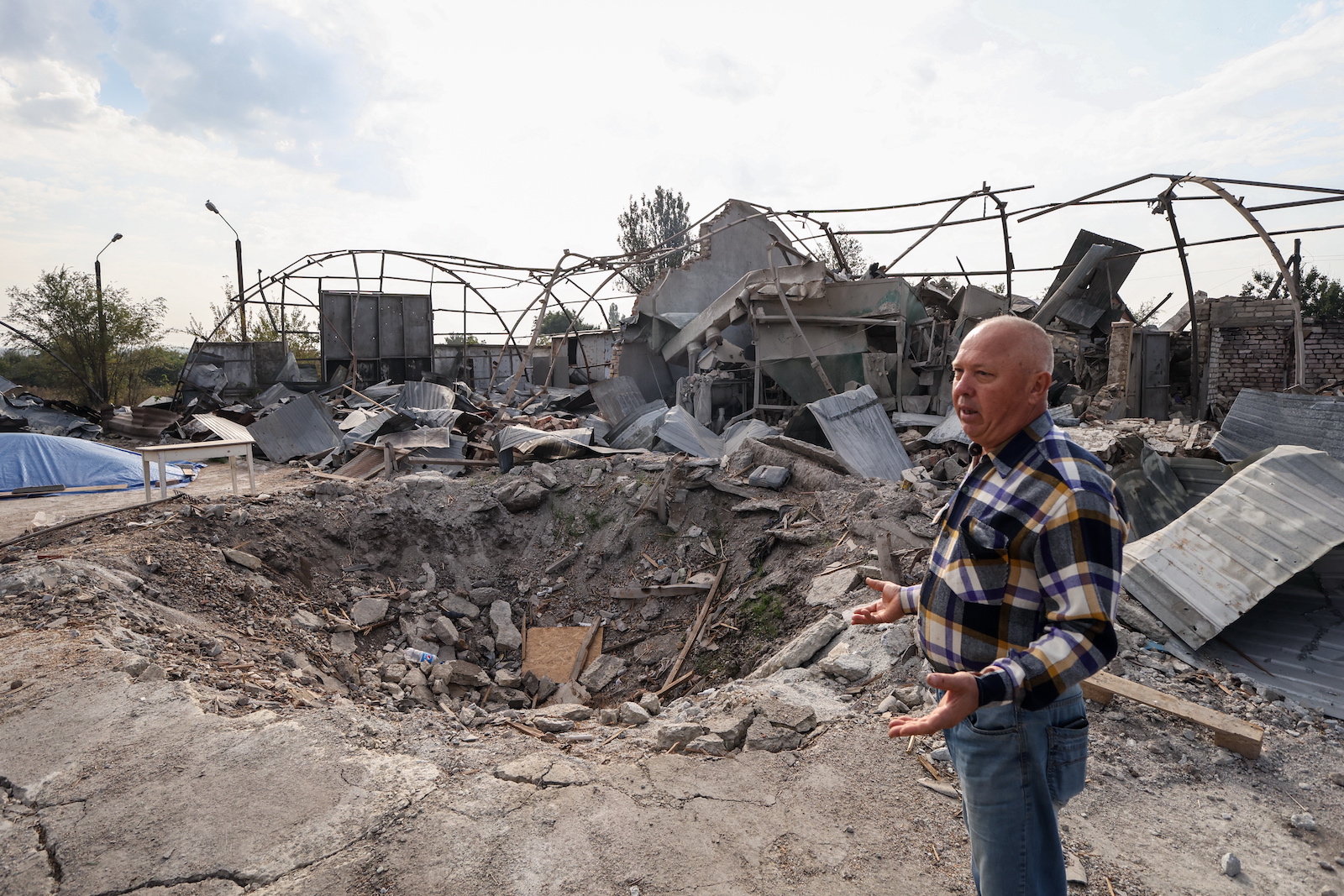 epa10860431 Ukrainian farmer Yakiv Marynchenko, 67, stands in front of a shell crater and a destroyed hangar with agricultural machinery on his farm, near the frontline town of Orikhiv, Zaporizhzhia region, southeastern Ukraine, 14 September 2023. Ukrainian farmer Yakiv Marynchenko, who owns the farm since 1995, cultivates sunflowers, wheat and other grains. He also owned a mill, but it was destroyed when Russian shelling hit his farm at the end of August 2023. The war in Ukraine has significantly impacted food security at the national and global levels, posing a threat to the worldwide food supply, according to the Food and Agriculture Organization of the United Nations (FAO). Russian troops entered Ukrainian territory in February 2022, starting a conflict that has provoked destruction and a humanitarian crisis.  EPA/KATERYNA KLOCHKO