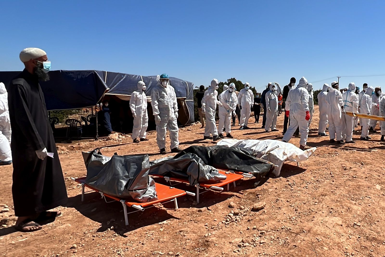 epa10865292 Rescuers stand near bodies of victims who died after Storm Daniel swept across eastern Libya, before burying the victims in mass graves, in the port city of Derna, eastern Libya, 16 September 2023. Unprecedented floods struck Libya after Mediterranean Storm Daniel made landfall on 10 September. Intense rainfall from the storm in the country's eastern region caused the collapse of two dams south of the city of Derna, sweeping away entire neighborhoods. The death toll has surpassed 11,000 and over 34,000 people have been displaced across the country. The flooding exacerbated Libya's needs, where 800,000 people are reported in need of humanitarian assistance, the International Rescue Committee (IRC) said.  EPA/STRINGER