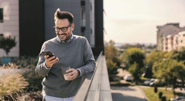 An urban businessman is enjoying coffee and internet while smiling on the phone downtown.