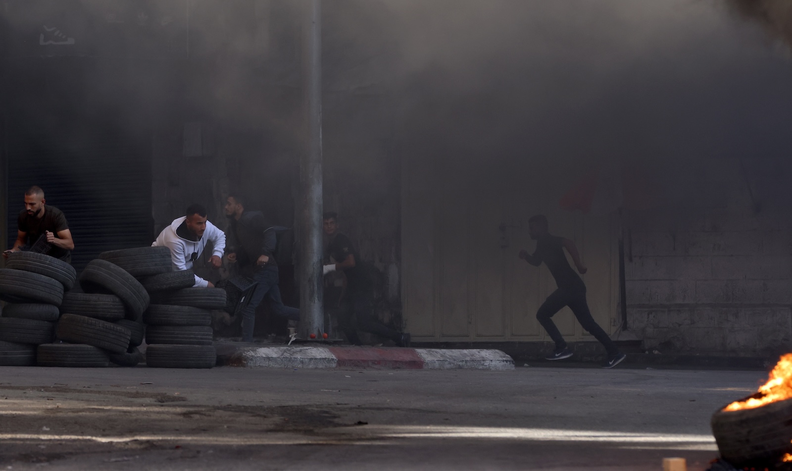 epa10966285 Palestinians take cover behind tires during clashes with Israeli troops following an Israeli raid at the Jenin refugee camp, in the West Bank city of Jenin, 09 November 2023. According to the Palestinian Health Ministry, at least nine Palestinians were killed and around 15 others were injured during heavy clashes with Israeli troops. Since 07 October 2023, more than 160 Palestinians have been killed, while over 2,000 have sustained injuries in the West Bank.  EPA/ALAA BADARNEH