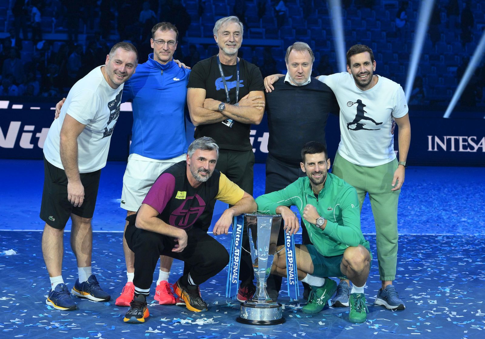epa10985382 Novak Djokovic of Serbia (bottom R), his coaches Goran Ivanisevic (bottom L) and Marco Panichi (R), and team members pose with the trophy after winning his singles finals match against Jannik Sinner of Italy at the Nitto ATP Finals tennis tournament in Turin, Italy, 19 November 2023.  EPA/ALESSANDRO DI MARCO