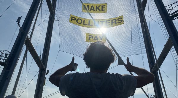 epaselect epa10988766 A crew member of the Greenpeace ship Rainbow Warrior gestures at a banner that reads 'Make Polluters Pay' while docked at the Port of Manila, Philippines, 22 November 2023. The Rainbow Warrior ship is in the Philippines to amplify stories of communities struggling with the climate crisis and to demand the government make polluters pay for their role in worsening climate change.  EPA/FRANCIS R. MALASIG