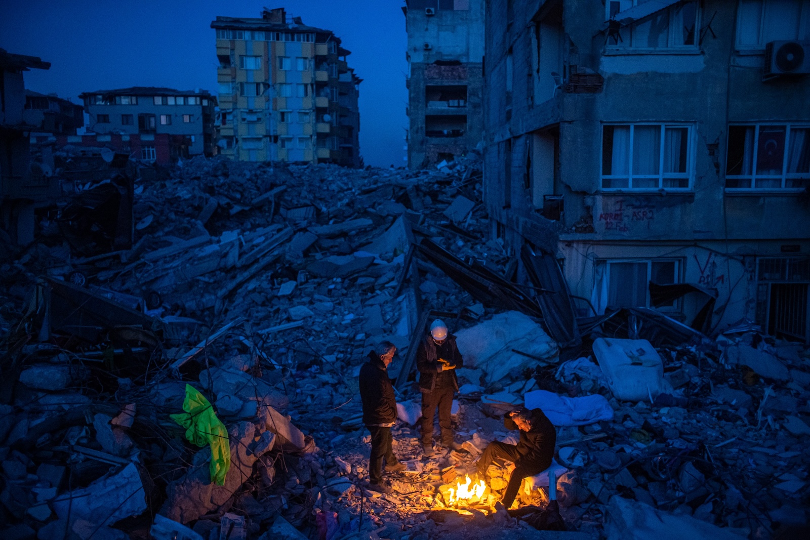 epa11000742 People gather by fire on debris of collapsed buildings after a powerful earthquake, in Hatay, Turkey, 15 February 2023. More than 50,000 people have died and more than 100,000 others were injured after two major earthquakes struck southern Turkey and northern Syria on 06 February 2023.  EPA/MARTIN DIVISEK