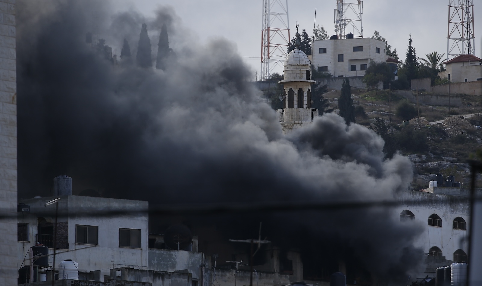 epa11026838 Smoke rises over residential buildings as the Israel Defence Force conduct a raid for the second day at a refugee camp near the West Bank city of Jenin, 13 December 2023. According to the Palestinian Health ministry, eight Palestinians were killed in Jenin during an Israeli military raid on 12 December. Thousands of Israelis and Palestinians have died since the militant group Hamas launched an unprecedented attack on Israel from the Gaza Strip on 07 October, and the Israeli operations in Gaza and the West Bank which followed it.  EPA/ALAA BADARNEH