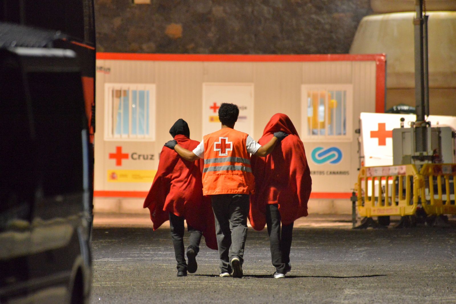 epa11028171 A Red Cross member helps two migrants after a boat, with 72 migrants on board, managed to reach La Restinga port, in El Hierro island, Canary Islands, southwestern Spain, late 13 December 2023 (issued on 14 December 2023). The boat was escorted to the port by a Spanish Civil Guard patrol boat after it was found off the coast.  EPA/Gelmert Finol