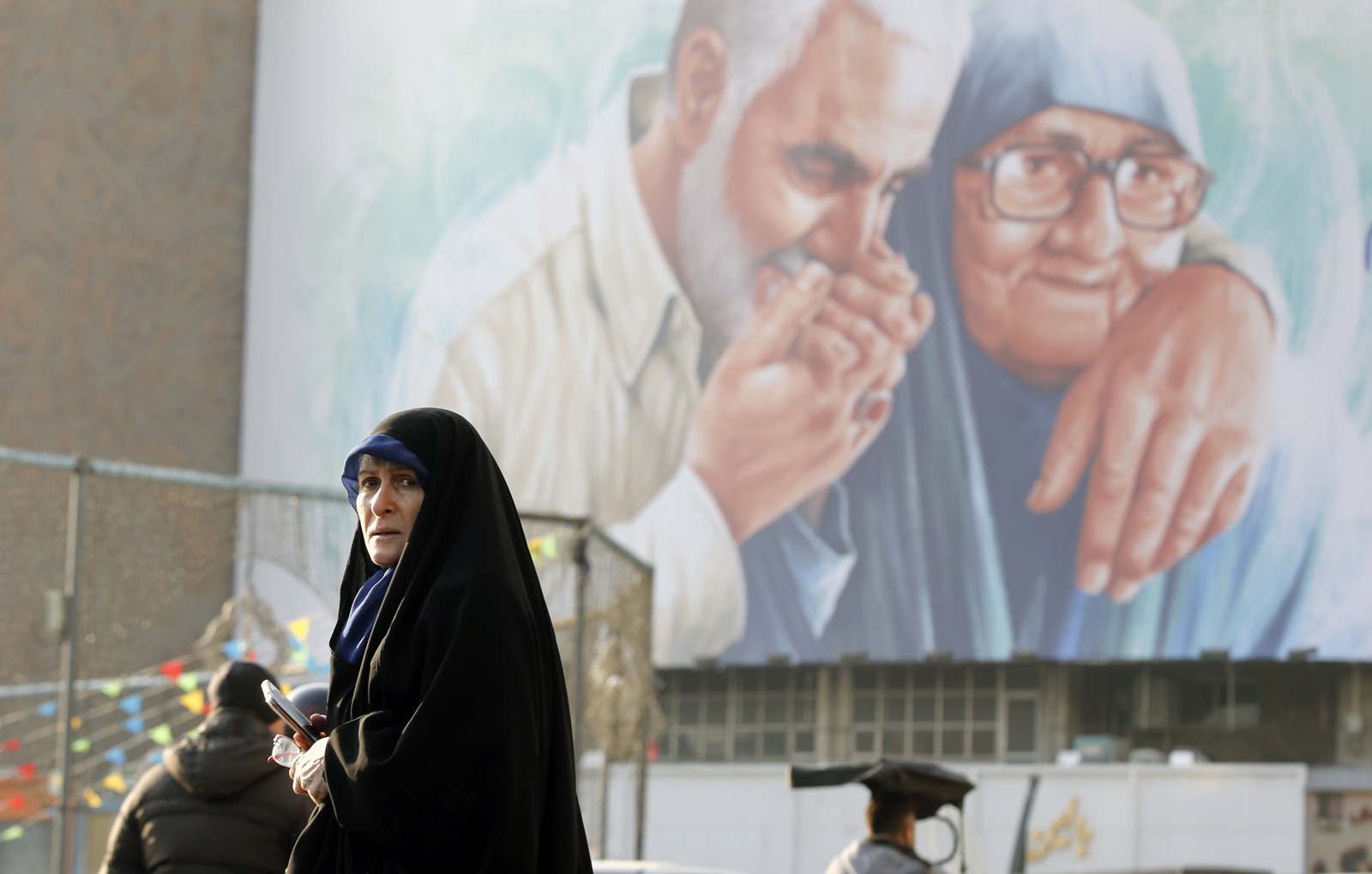 epa11053650 An Iranian woman walks past a huge billboard showing the late Iran's Islamic Revolutionary Guard Corps (IRGC) Quds Force commander Qasem Soleimani kissing his mother's hand in the Vali-Asr square ahead of his fourth death anniversary, in Tehran, Iran, 02 January 2024. Iranians will mark the anniversary of Soleimani's death on 03 January 2024. Soleimani was killed on 03 January 2020 in a targeted US airstrike at the Baghdad airport in Iraq.  EPA/ABEDIN TAHERKENAREH