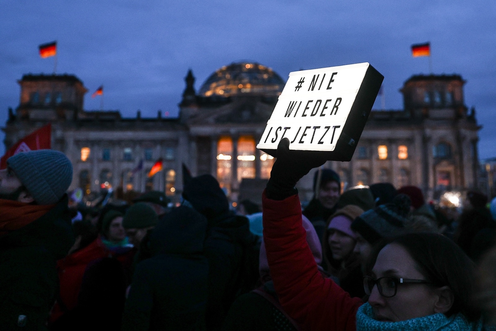 epa11094570 A protester holds a sign reading 'never again is now' in front of German parliament Bundestag, during a demonstration against the far-right Alternative for Germany (AfD) party in Berlin, Germany, 21 January 2024. The protest held under the slogan 'Defend Democracy', was organized by the Fridays for Future movement, along with other non-governmental organizations, as a reaction to revelations of the investigative journalism group Correctiv, and their report about a meeting of far-right politicians, who allegedly discussed deportation plans referred to as 'remigration', a term promoting the forced return of 'migrants' to their place of origin.  EPA/FILIP SINGER