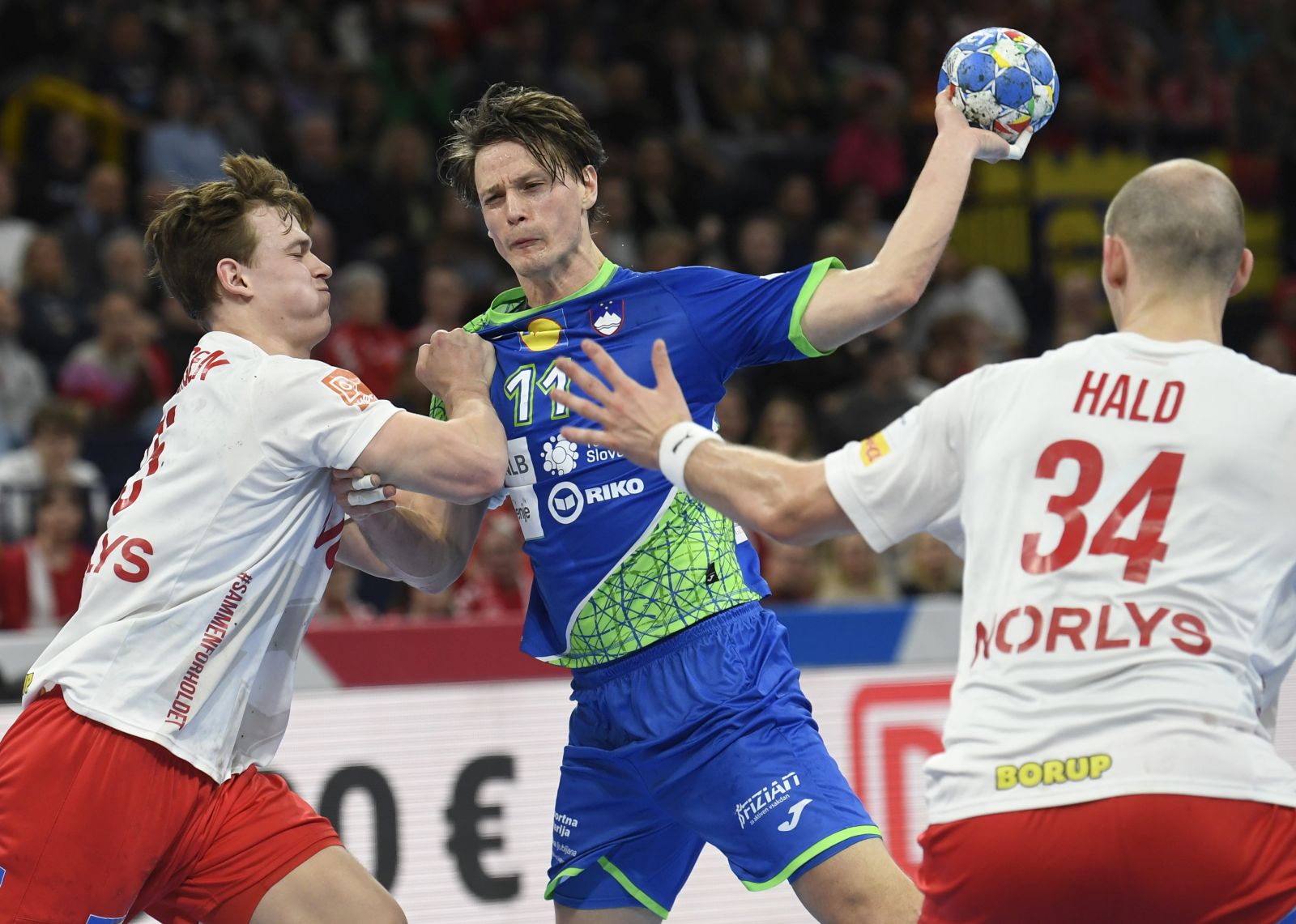 epa11099267 Slovenia’s Joe Delenec (C) and Denmark’s Lukas Jorgensen (L) and Simon Hald (R) in action during the EHF Men's EURO 2024 main round handball match between Slovenia and Denmark in Hamburg, Germany, 23 January 2024.  EPA/FABIAN BIMMER