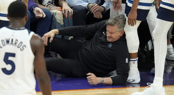 Minnesota Timberwolves head coach Chris Finch holds his knee after colliding with Timberwolves guard Mike Conley during the second half of Game 4 of an NBA basketball first-round playoff series against the Phoenix Suns Sunday, April 28, 2024, in Phoenix. The Timberwolves won 122-116, taking the series 4-0. (AP Photo/Ross D. Franklin)