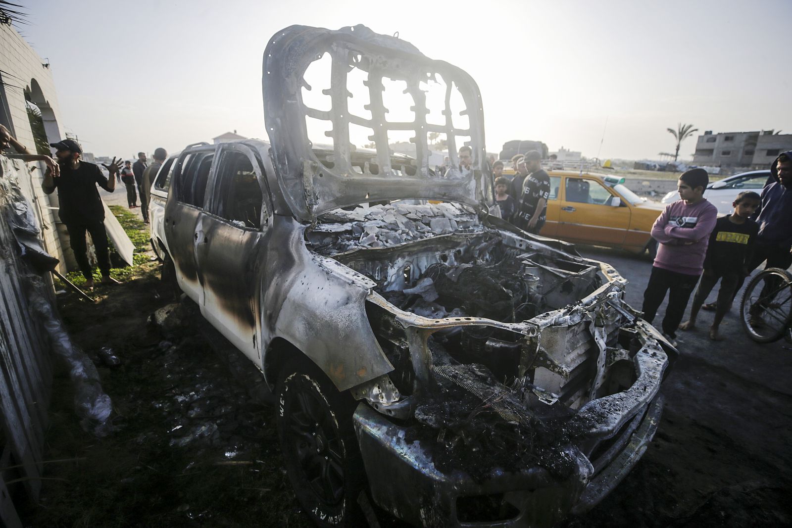 epa11255142 People stand near a destroyed car of the NGO World Central Kitchen (WCK) along Al Rashid road, between Deir Al Balah and Khan Younis in the southern Gaza Strip, 02 April 2024. According to the Palestinian Red Crescent, at least four people from the NGO World Central Kitchen (WCK) were killed when a missile hit their convoy in Deir al Balah while they were on their way from Rafah to Gaza City to receive fresh aid delivered by the Open Arms vessel. The victims were confirmed to be a British, a Polish and an Australian citizen, while the nationality of the fourth victim was still unknown.  EPA/MOHAMMED SABER