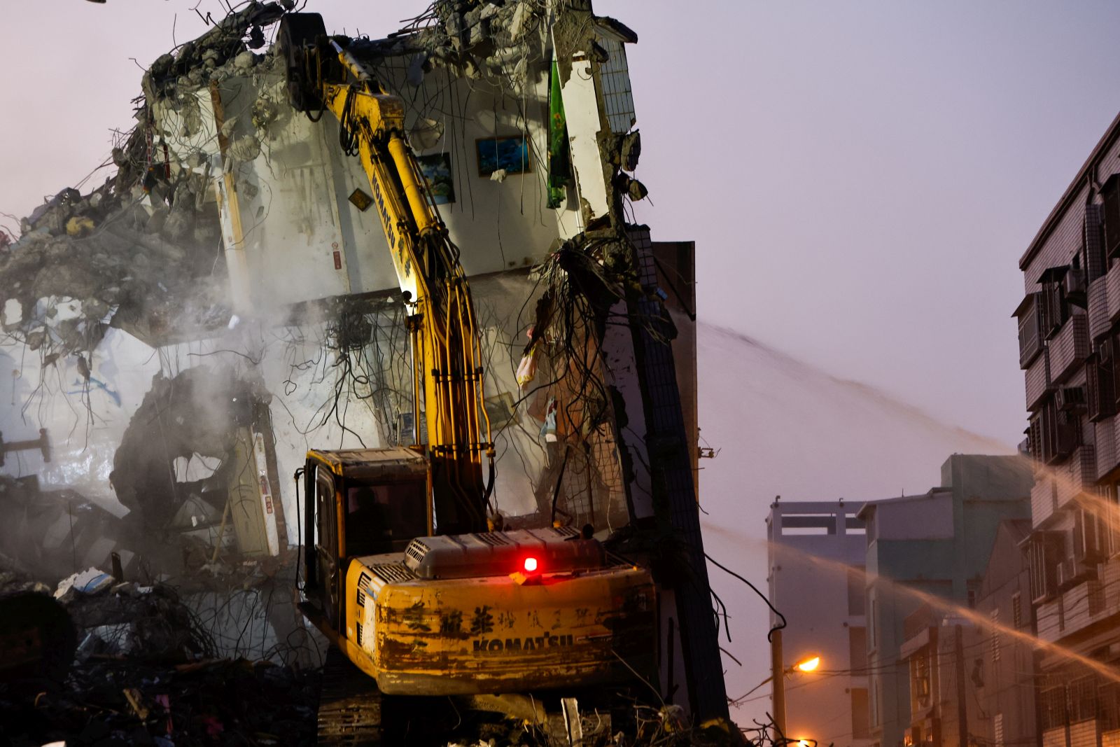 epa11257844 Firefighters spray water while an excavator demolishes the wreckage of a collapsed residential building following the 03 April magnitude 7.4 earthquake in Hualien, Taiwan, 04 April 2024. According to data released by Taiwan's National Fire Agency, the earthquake has taken at least nine lives and injured hundreds, making it the strongest earthquake in 25 years.  EPA/DANIEL CENG