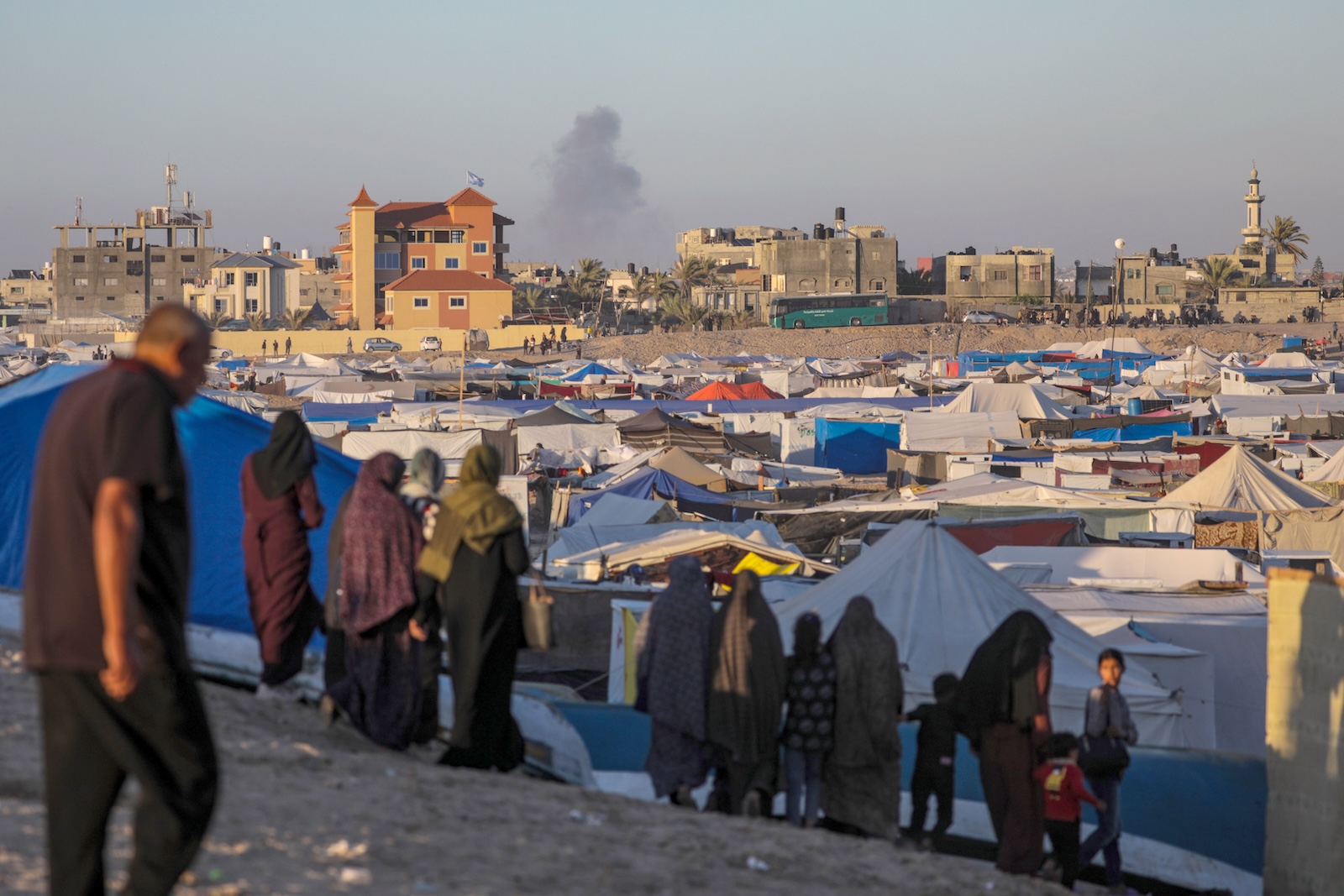 epaselect epa11326105 Internally displaced Palestinians stand at a camp as smoke rises in the background after an Israeli air strike, in Rafah, southern Gaza Strip, 07 May 2024 (issued 08 May 2024). The Israel Defence Forces (IDF) on 06 May called on residents of eastern Rafah to 'temporarily' evacuate to an expanded humanitarian area. On 07 May the IDF stated that its ground troops began an overnight operation targeting Hamas militants and infrastructure within specific areas of eastern Rafah, taking operational control of the Gazan side of the Rafah crossing based on intelligence information. More than 34,600 Palestinians and over 1,455 Israelis have been killed, according to the Palestinian Health Ministry and the IDF, since Hamas militants launched an attack against Israel from the Gaza Strip on 07 October 2023, and the Israeli operations in Gaza and the West Bank which followed it.  EPA/MOHAMMED SABER