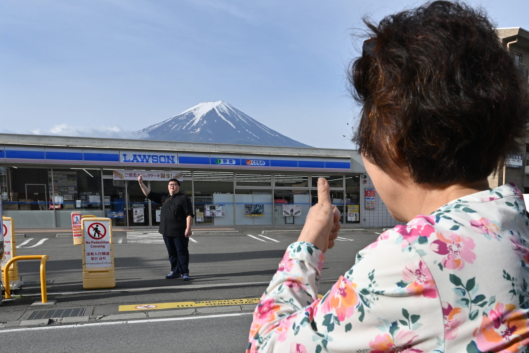 A person takes pictures of Mount Fuji from across the street of a convenience store, hours before the installation of a barrier to block the sight of Japan's Mount Fuji to deter badly behaved tourists, in the town of Fujikawaguchiko, Yamanashi prefecture on May 21, 2024. The plan to erect a large mesh barrier across the road from an Instagram-famous view of Mount Fuji made headlines last month when it was announced by officials fed up with what locals said were unending streams of mostly foreign visitors littering, trespassing and breaking traffic rules.,Image: 875012973, License: Rights-managed, Restrictions: , Model Release: no, Credit line: Kazuhiro NOGI / AFP / Profimedia