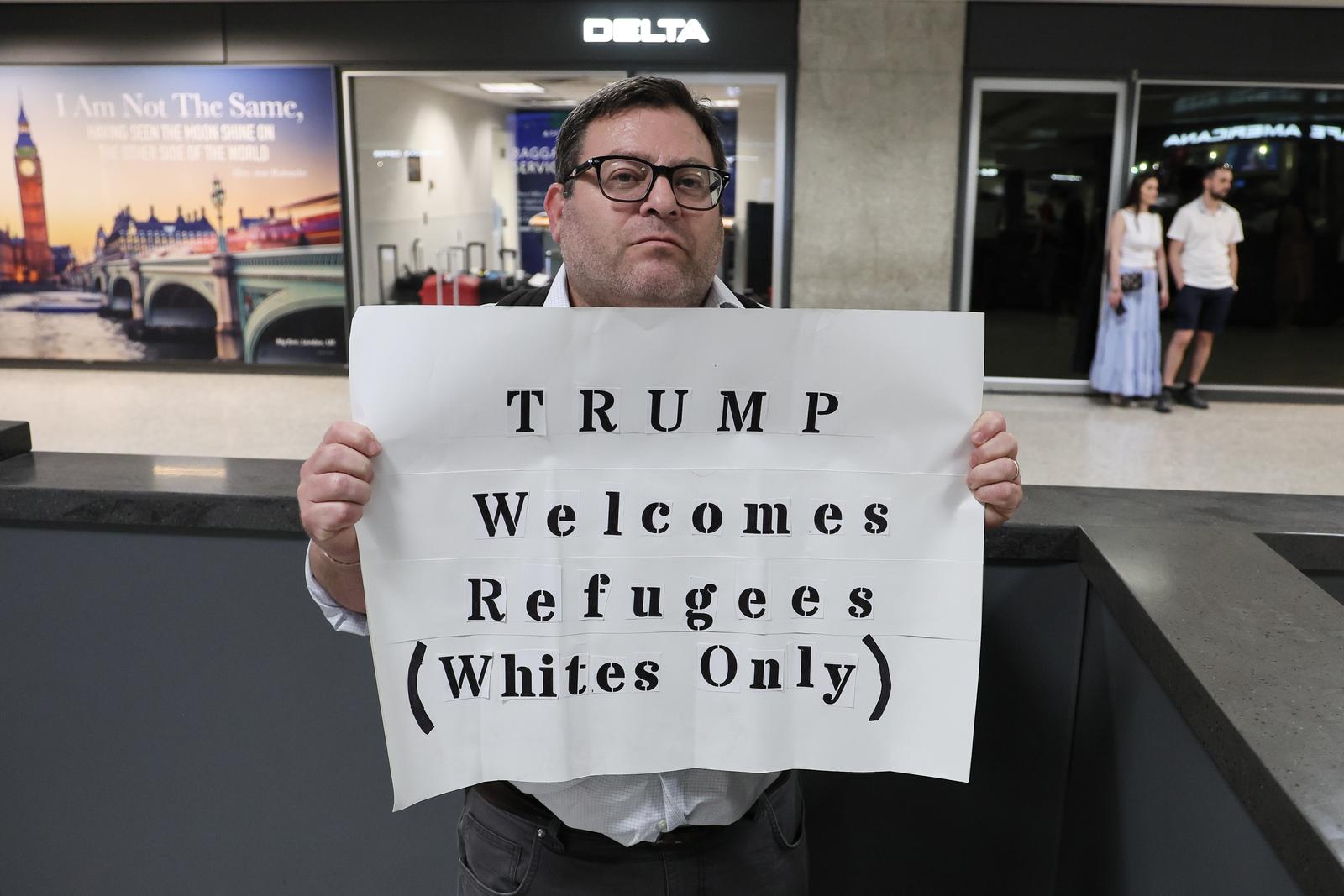 A protestor holds up a sign protesting President Trumps new policies towards refugees at the International Arrivals Terminal at Dulles International Airport as the first flight of Afrikaners From South Africa granted refugee status arrive in the United States on May 12, 2025 in Sterling, Virginia. The newly arriving Afrikaner immigrants underwent immigration processes that were expedited due to claims of oppression and genocide as the Trump administration halted immigration from other countries in the world affected by war or harsh socio-econiomic conditions. Photo by Jemal Countess/UPI Photo via Newscom Photo: Jemal Countess/NEWSCOM