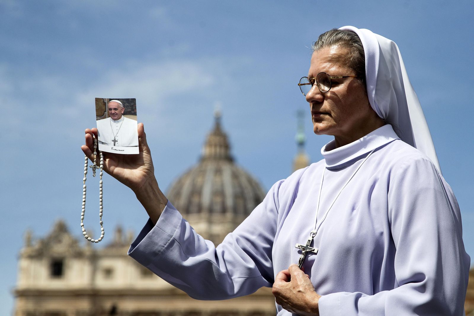 epa12044119 A nun carries a cross and a picture of Pope Francis as she prays in St. Peter's Square following the death of Pope Francis, Vatican City, 21 April 2025. Pope Francis died on 21 April 2025 at the age of 88, according to the Holy See. Born Jorge Mario Bergoglio in Buenos Aires, Argentina, on 17 December 1936, he was appointed leader of the Catholic Church on 13 March 2013, succeeding Pontiff Emeritus Benedict XVI.  EPA/ANGELO CARCONI