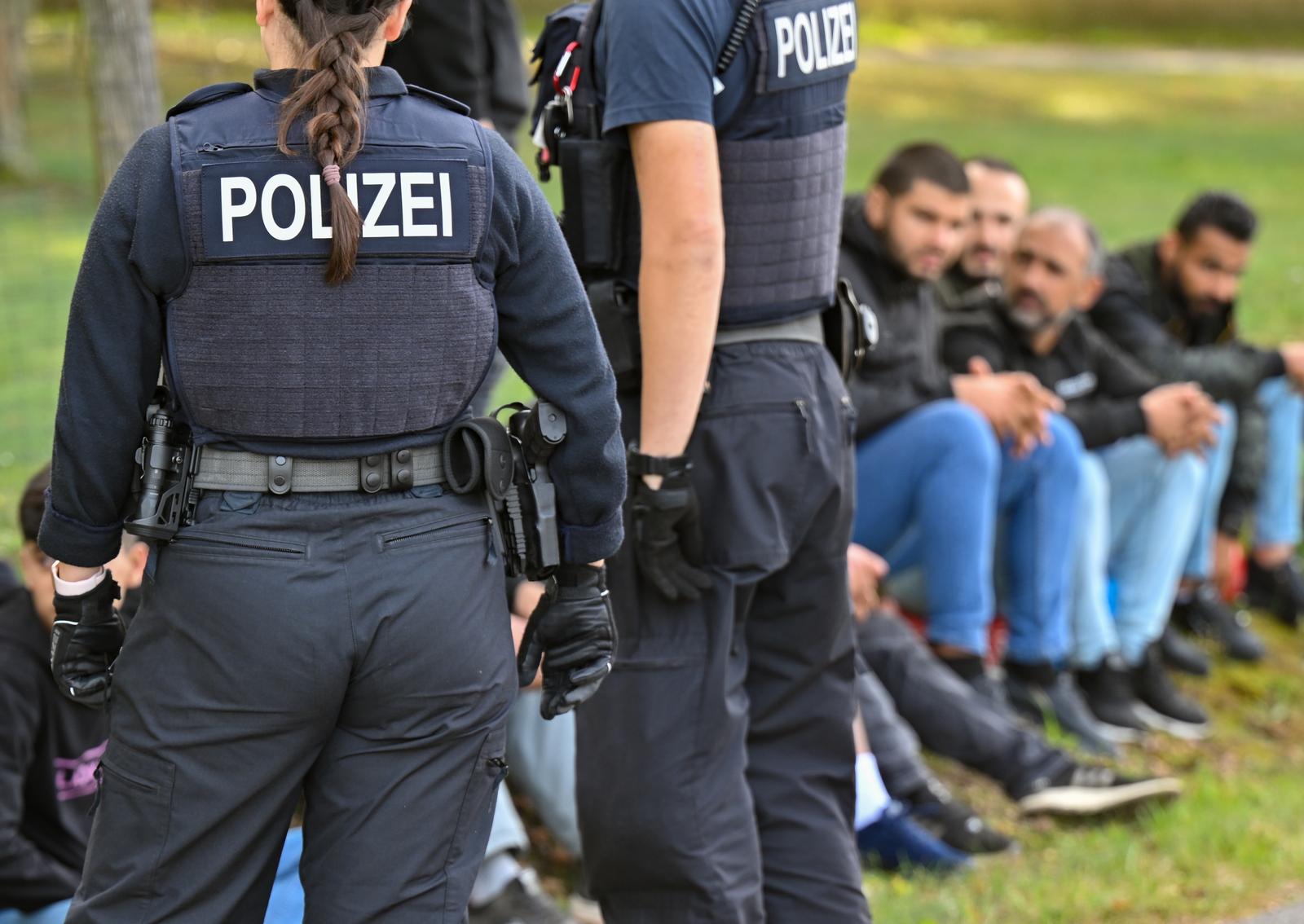 11 October 2023, Brandenburg, Forst: Illegal migrants are guarded by officers of the Federal Police during an apprehension near the German-Polish border in Forst (Lausitz). During several operations in Forst, Brandenburg, and the surrounding area, the Federal Police had apprehended at least 64 migrants who had entered the country without permission on Oct. 11, 2023. According to their own information, they were brought to Germany by smugglers via the so-called Balkan route from Turkey via Greece, Bulgaria, Hungary, Slovakia and Poland and dropped off shortly after the border. For several weeks now, the German Federal Police have been stepping up their search for criminals who bring refugees and migrants to Germany without permission by carrying out mobile checks at the German-Polish border. Photo: Patrick Pleul/dpa Photo: Patrick Pleul/DPA