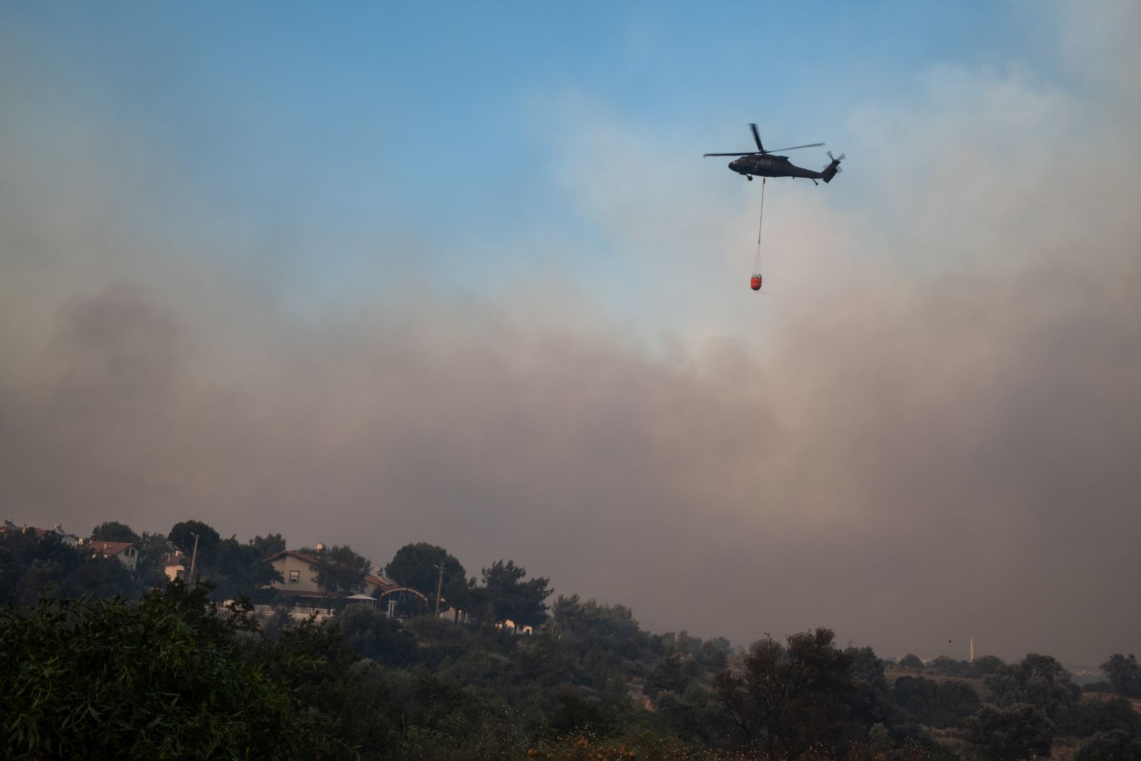 epa12207116 A helicopter carries water to put out the fire during the wildfires in the Seferihisar district of Izmir, Turkey, 30 June 2025. Turkish Forestry Minister Ibrahim Yumakli said the blaze in the Kuyucak and Doganbey areas of Izmir was fanned overnight by winds reaching 40–50 km/h (25–30 mph), leading to the evacuation of four villages and two neighbourhoods.  EPA/MURAT KOCABAS