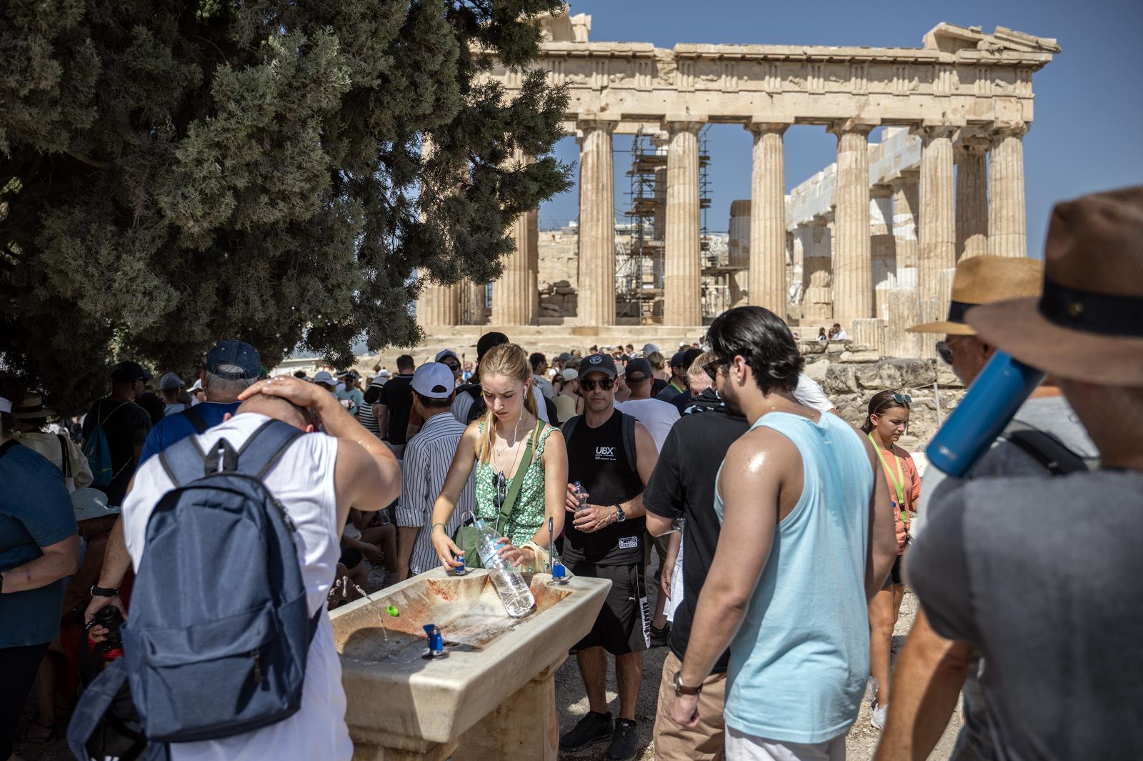 14 July 2023, Greece, Athen: Tourists cool off at a water fountain during their visit to the Parthenon Temple on the Acropolis Hill on this hot day. The Ministry of Culture has decided to close the archaeological site during the hottest hours of the day, from noon to 5 p.m., as Greece is currently experiencing a heat wave. Photo: Angelos Tzortzinis/dpa Photo: ANGELOS TZORTZINIS/DPA