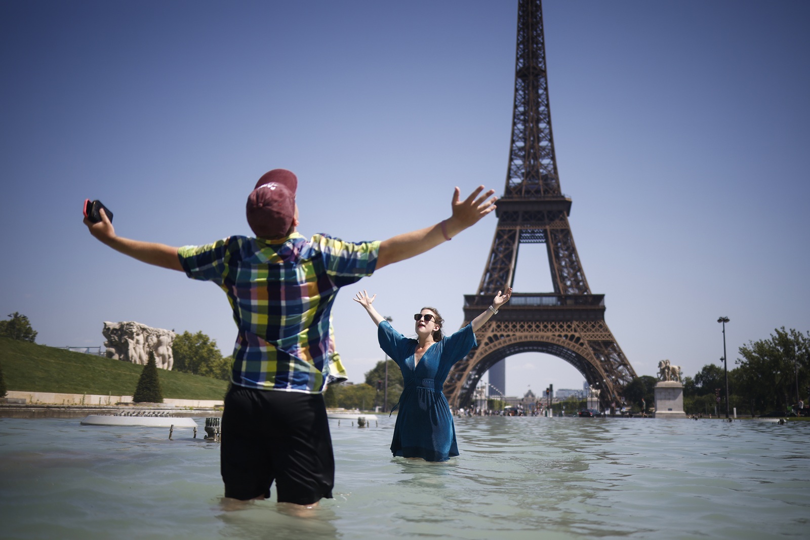 epa12208719 People cool off with water from Varsovie fountain by the Eiffel Tower during a heatwave in Paris, France, 01 July 2025. The hottest day of this heatwave on 01 July 2025, will register temperatures peaking into 40-41 degrees Celsius, in several departments, according to Meteo France.  EPA/YOAN VALAT