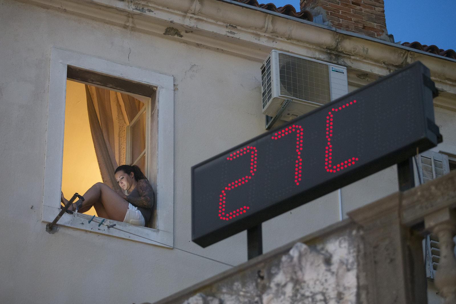 12.07.2015., Split - Uvecer kada temperature barem malo padnu mnogi se turisti kao i domaci ljudi odluce na setnju Marmontovom ulicom u Splitu. Djevojka na prozoru cita s mobitela dok panel za mjerenje temperature pokazuje 27 stupnjeva celziusa.r"n Photo: Davor Puklavec/PIXSELL