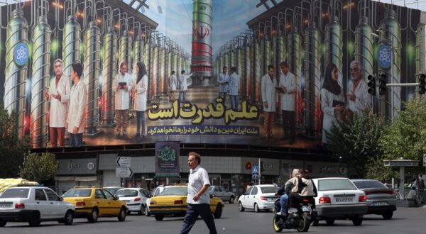 epa12342275 An Iranian man crosses a road near a billboard displaying a picture of nuclear centrifuges and a sentence reading in Persian 'Science is the power, and the Iranian nation will not abandon its religion and knowledge' at the Enghelab square in Tehran, Iran, 01 September 2025.  EPA/ABEDIN TAHERKENAREH