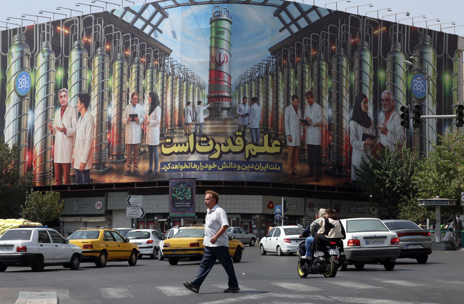 epa12342275 An Iranian man crosses a road near a billboard displaying a picture of nuclear centrifuges and a sentence reading in Persian 'Science is the power, and the Iranian nation will not abandon its religion and knowledge' at the Enghelab square in Tehran, Iran, 01 September 2025.  EPA/ABEDIN TAHERKENAREH