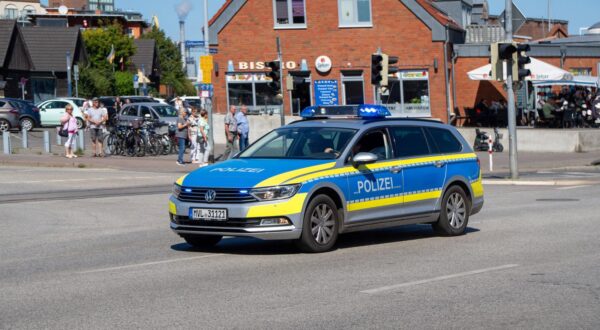 Wismar, Deutschland 19.Aug.2025: Im Bild: Polizeifahrzeug Volkswagen Passat Variant mit blauer und gelber Lackierung und eingeschaltetem Blaulicht im Einsatz in der Innenstadt von Wismar, Polizei Mecklenburg-Vorpommern, Sicherheitskräfte im Streifendienst, sichtbare Polizeipräsenz im Stadtverkehr, Verkehrssicherheit, Kontrolle, Einsatz gegen Kriminalität, Streifenwagen vor Bistro am Hafen und Passanten im Hintergrund. Mecklenburg Vorpommern *** Wismar, Germany 19 Aug 2025 In the picture police car Volkswagen Passat Variant with blue and yellow paintwork and switched on blue light in action in the city center of Wismar, police Mecklenburg Vorpommern, security forces on patrol duty, visible police presence in city traffic, traffic safet Copyright: xFotostandx/xGelhotx Photo: IMAGO/Fotostand / Gelhot/IMAGOSTOCK&PEOPLE