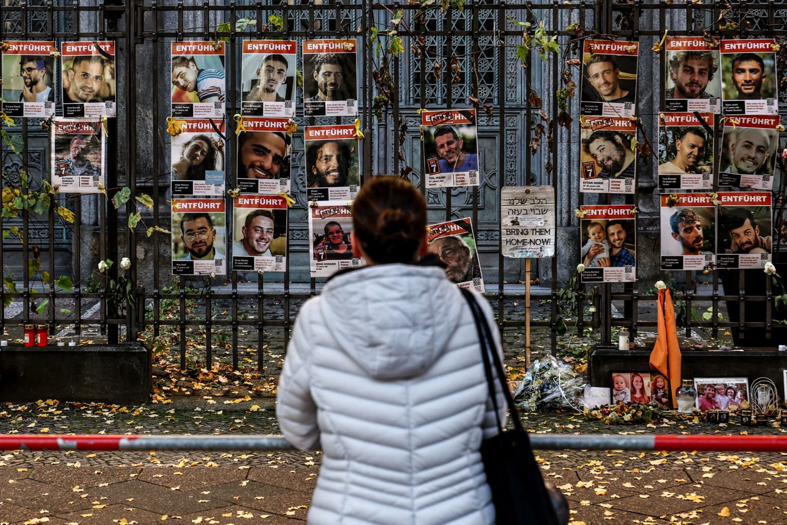epa12451253 A pedestrian looks on at portraits of Israeli hostages and victims displayed on a fence in front of the New Synagogue in Berlin, Germany, 13 October 2025. The first phase of the Gaza peace agreement, reached between Israel and Hamas, includes the release of Israeli hostages and Palestinian prisoners, a partial withdrawal of Israeli forces, and the delivery of humanitarian aid to Gaza.  EPA/FILIP SINGER
